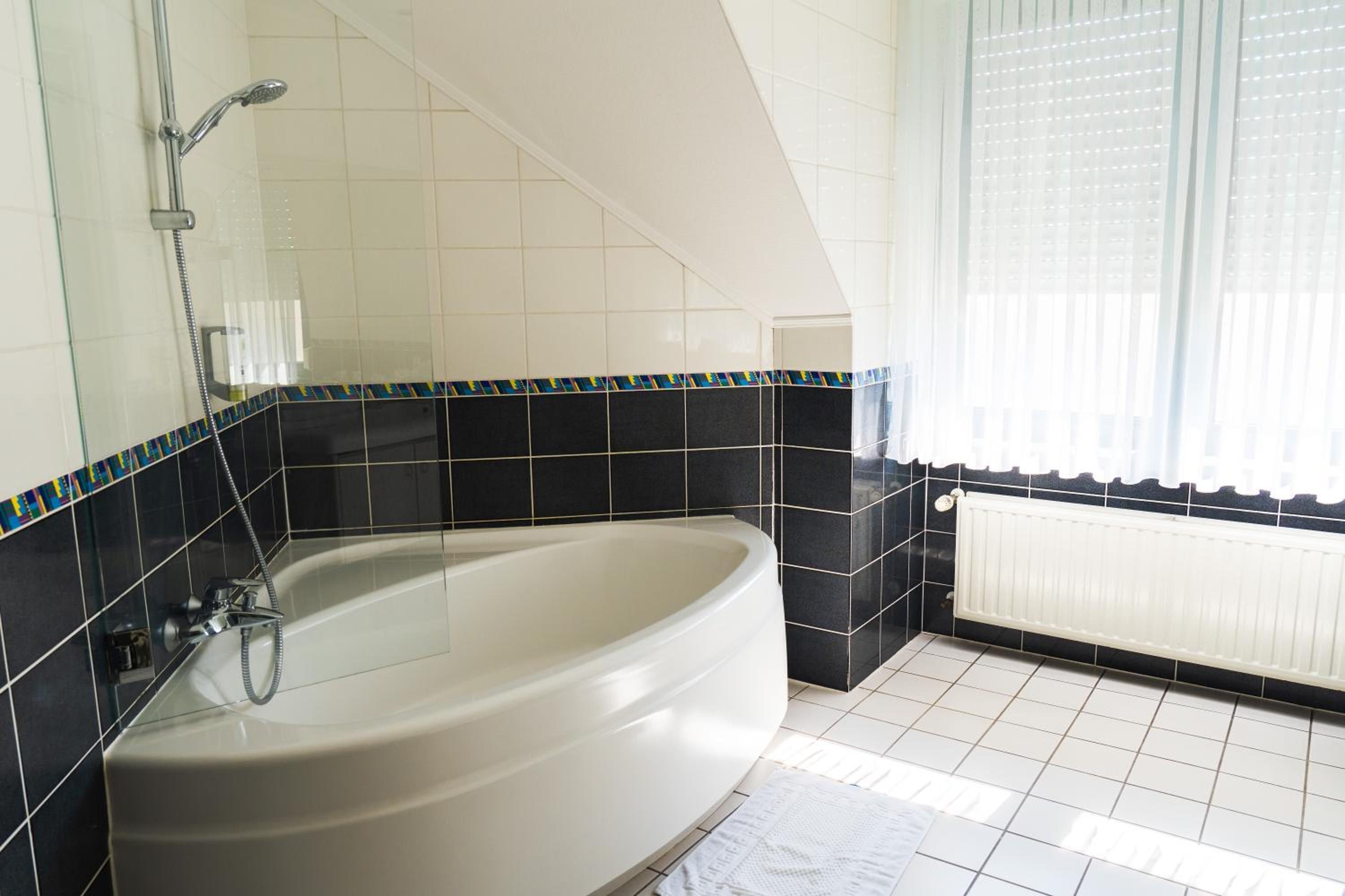 Ein Badezimmer mit freistehender Badewanne, einer Dusche und einem Fenster mit Jalousien.