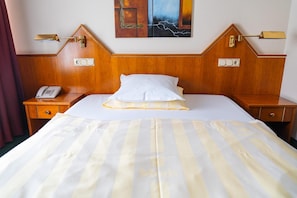 A hotel room with a wooden headboard, a bed with white and yellow striped bedding, a bedside telephone, and wall-mounted light fixtures. - Hotel Restaurant Moris (Walferdange)