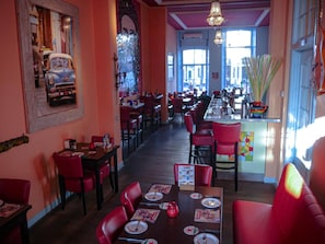 Un restaurante con sillas y mesas rojas, una zona de bar y grandes ventanales que dejan entrar luz natural.
