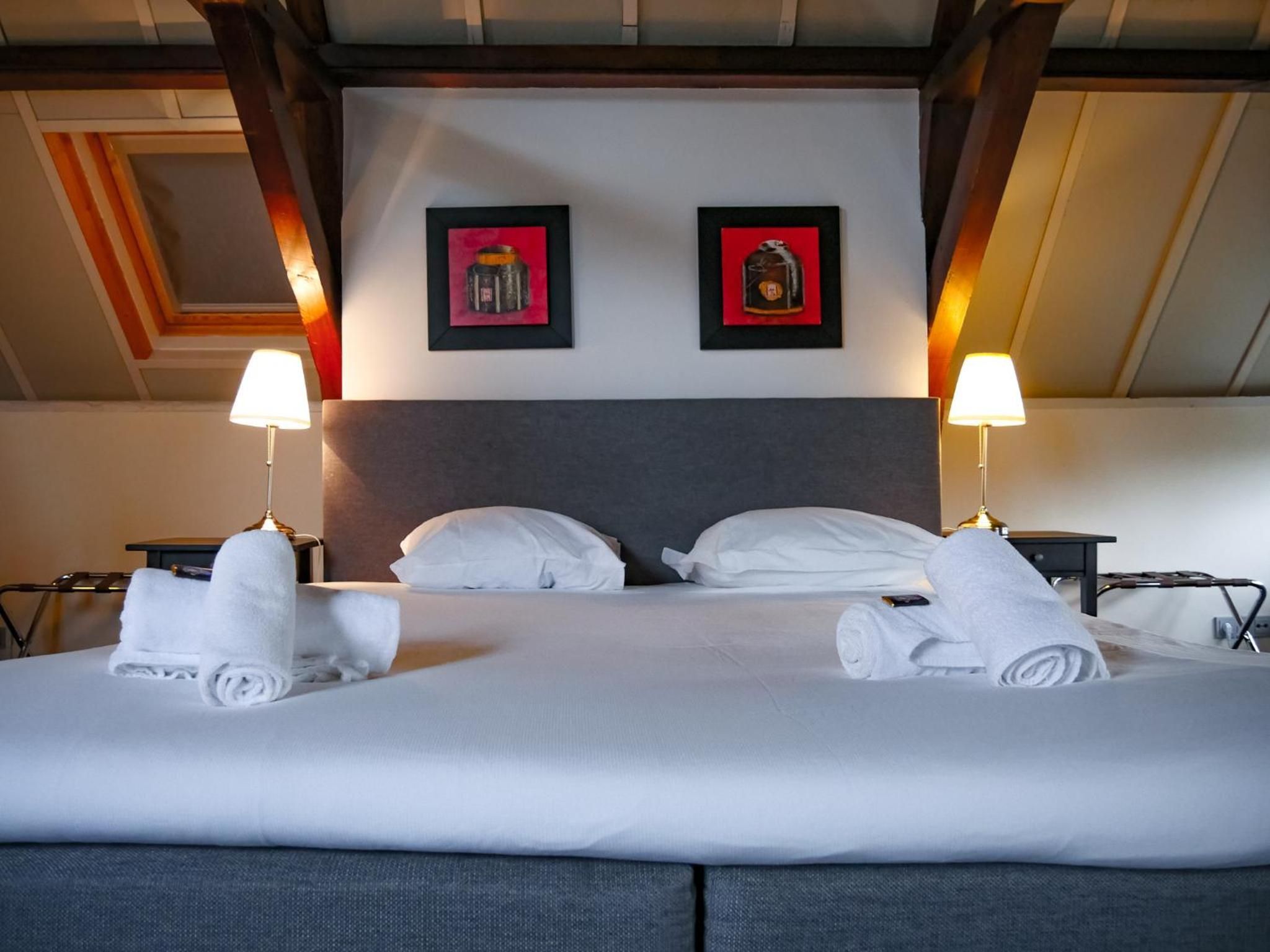 Quarto de hotel com uma cama grande, duas luminárias de cabeceira e duas quadros na parede.
