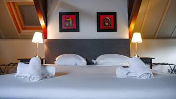 Quarto de hotel com uma cama grande, duas luminárias de cabeceira e duas quadros na parede.