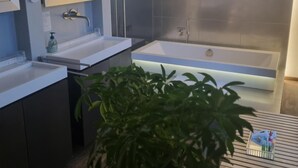 Un baño moderno con lavamanos doble, una bañera grande y un box de ducha.