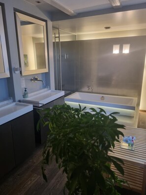Un baño moderno con lavamanos doble, una bañera grande y un box de ducha.
