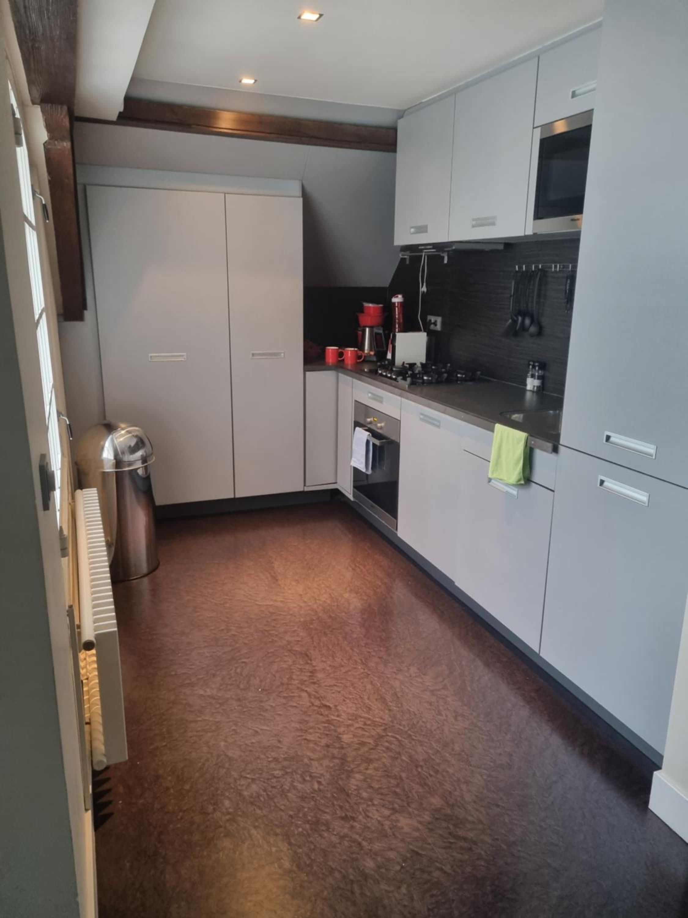 Eine kompakte Küche mit einem Einbauofen, einer Kaffeemaschine und einem Edelstahl-Mülleimer.