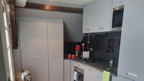 Una cocina compacta con horno integrado, cafetera y un cubo de basura de acero inoxidable.