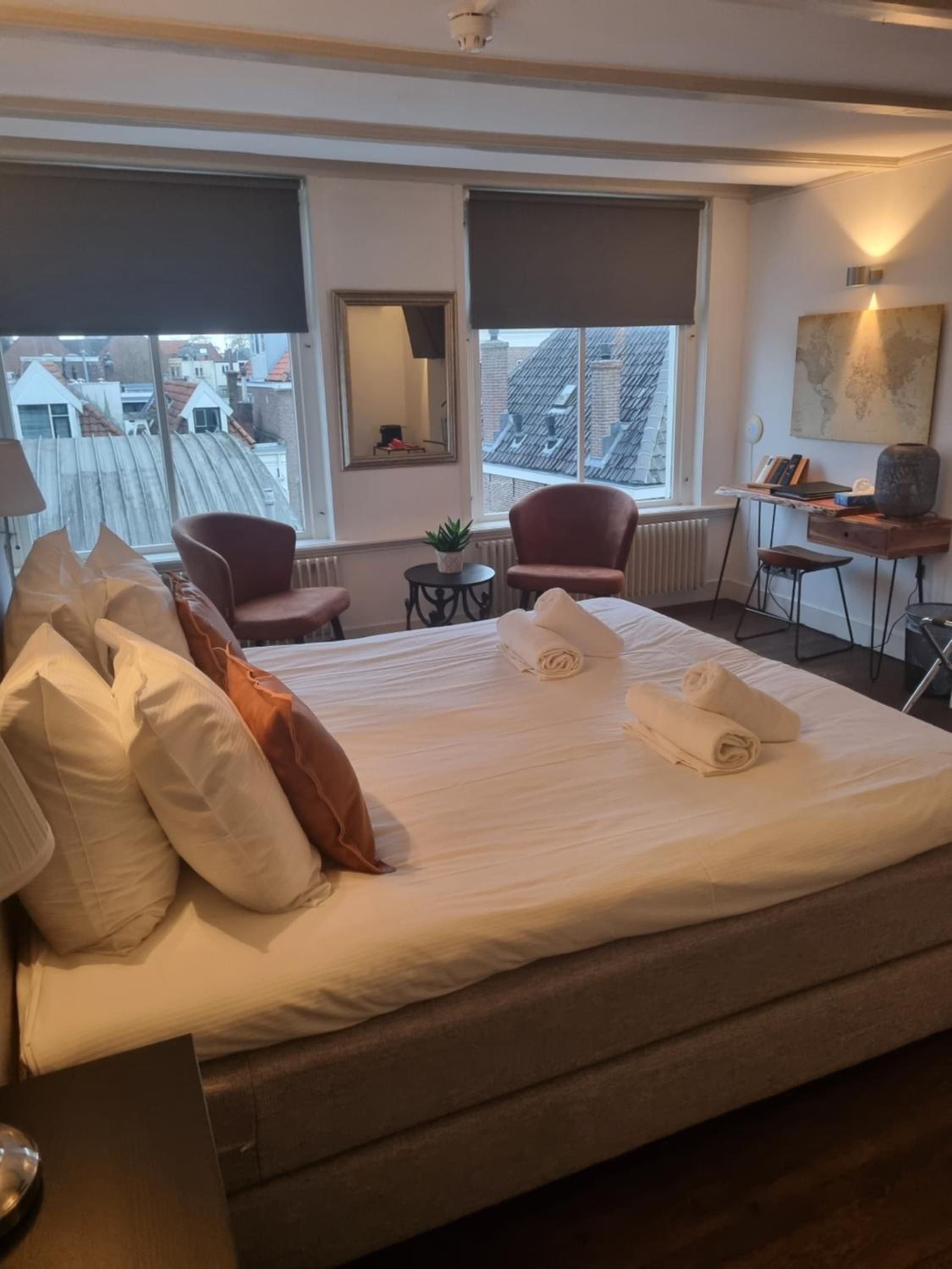 Quarto de hotel com uma cama grande, uma escrivaninha, uma cadeira e vista para a paisagem urbana.