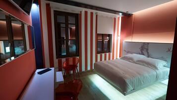 Habitació d'hotel amb un llit, una taula de treball amb cadira, una finestra i una porta.