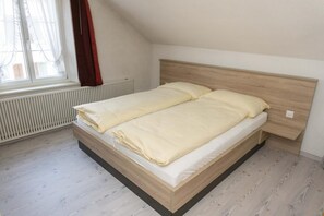 A single bed in a room with a sloped ceiling, a radiator, and a window with curtains. - Speiserestaurant Traube (Küttigen)