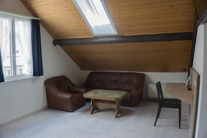 Ein Loft-Zimmer mit schrägem Dach, einem braunen Ledersofa, einem Holztisch und einem Esstisch mit Stühlen.