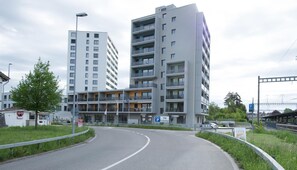 Un edificio de varios pisos con balcones, un letrero de estacionamiento y una carretera curva.