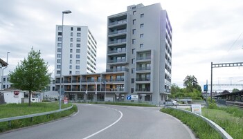 A multi-story building with balconies, a parking sign, and a curved road.