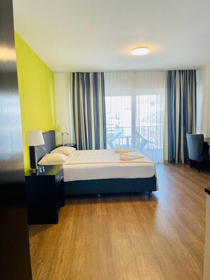 Habitación de hotel con cama, escritorio, silla y vista al exterior.
