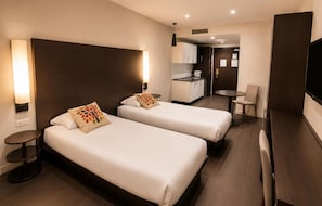 Quarto de hotel com duas camas, uma kitchenette pequena, área de refeições e uma TV.