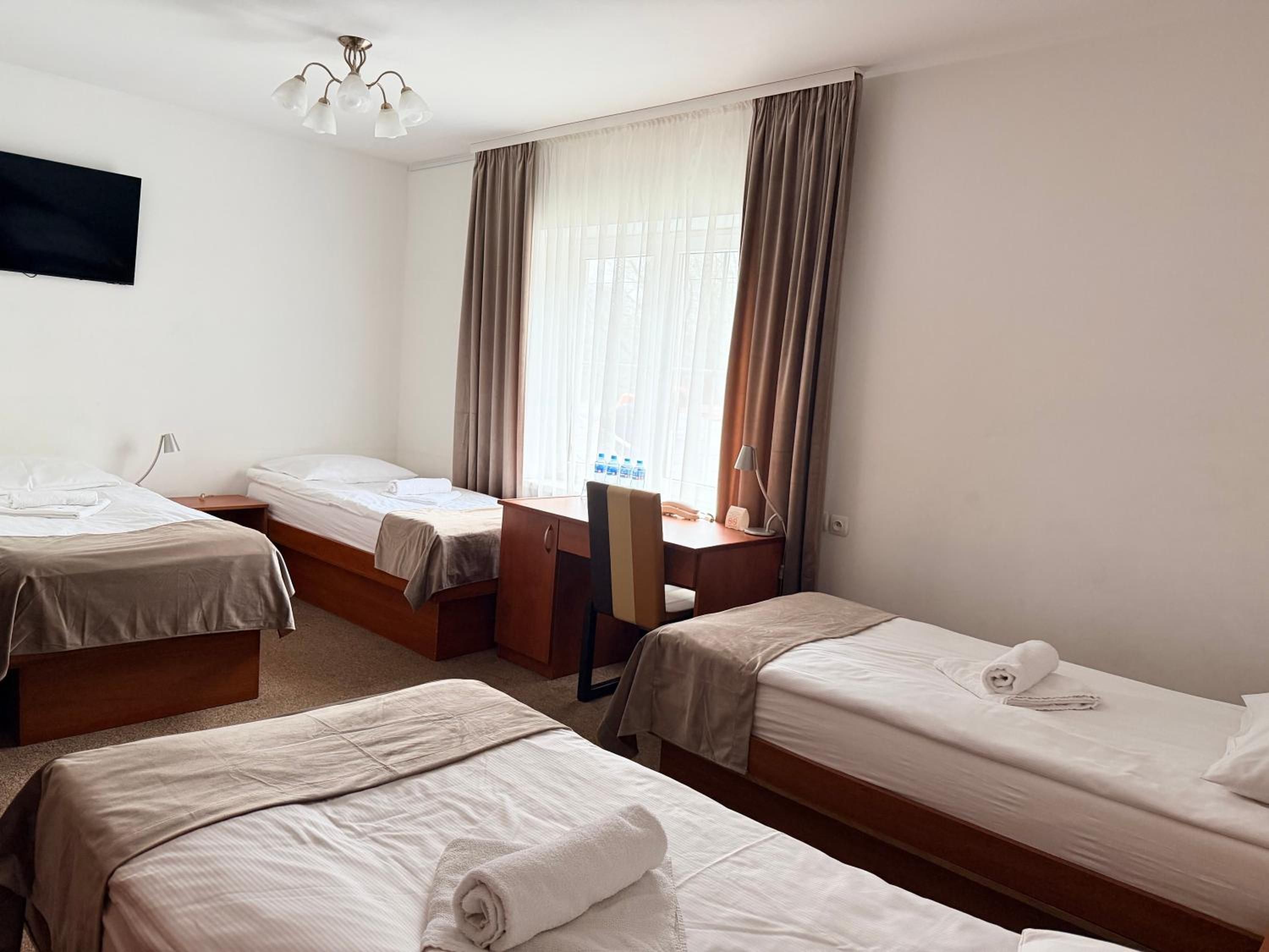 A hotel room with two single beds, a desk, a chair, and a television mounted on the wall.