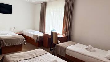 A hotel room with two single beds, a desk, a chair, and a television mounted on the wall.