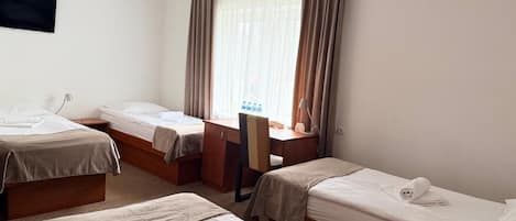 A hotel room with two single beds, a desk, a chair, and a television mounted on the wall.