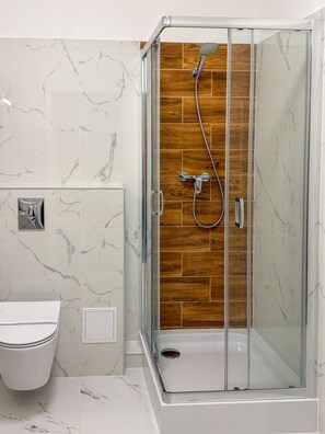 A glass-enclosed shower with a wooden panel wall, a white toilet, and marble-patterned tiles. - Hotel Sjesta (Mikołów)