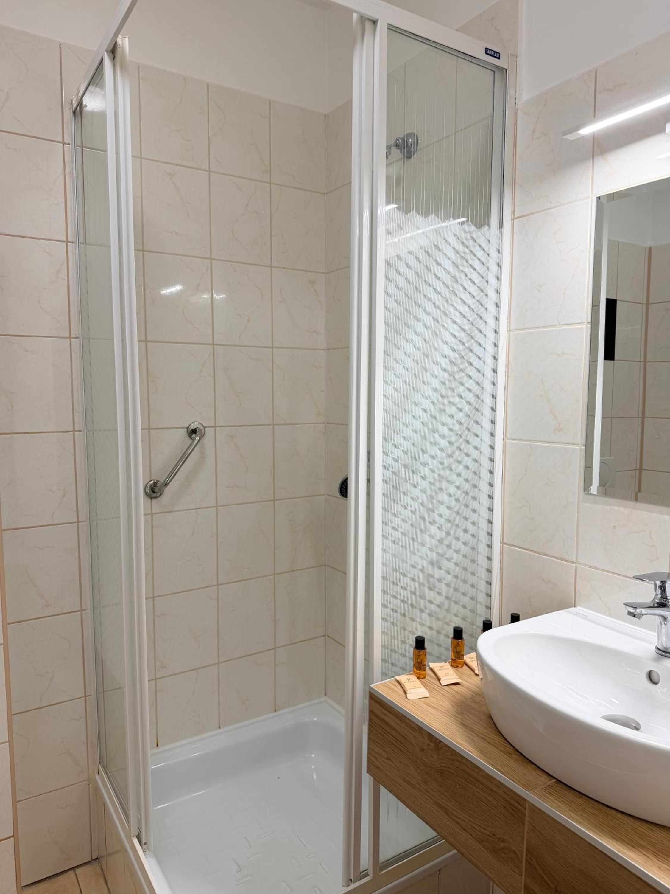 A modern bathroom with a glass-enclosed shower, a white bathtub, and a wooden vanity with a sink.