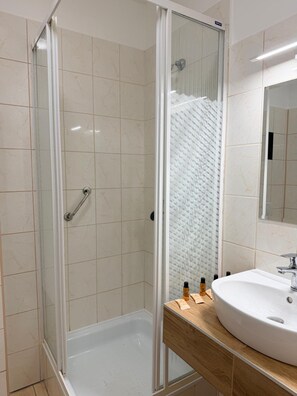 A modern bathroom with a glass-enclosed shower, a white bathtub, and a wooden vanity with a sink. - Hotel Sjesta (Mikołów)