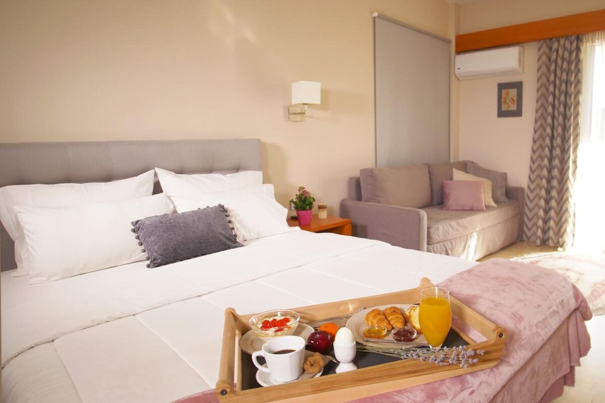 A hotel room with a bed, a side table with a lamp, a sofa, and a breakfast tray with food and drinks.