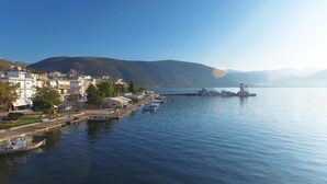 A waterfront town with buildings along the shore, a calm body of water, and a hilly landscape in the background. - Antikyra Beach Hotel (Distomo-Arachova-Antikyra)