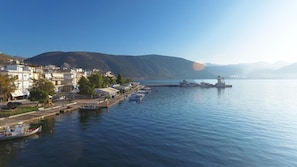 A waterfront town with buildings along the shore, a calm body of water, and a hilly landscape in the background. - Antikyra Beach Hotel (Distomo-Arachova-Antikyra)