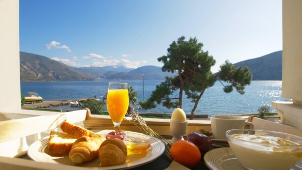 A breakfast table with croissants, orange juice, and a view of a lake with mountains in the background. - Antikyra Beach Hotel (Distomo-Arachova-Antikyra)