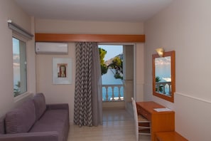 A room with a sofa, a desk, a chair, a window with a view of the sea, and a balcony. - Antikyra Beach Hotel (Distomo-Arachova-Antikyra)