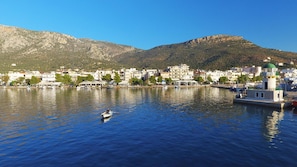 A coastal town with buildings along the waterfront, a boat in the water, and mountains in the background.
