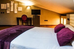 A hotel room with a bed, a desk, a chair, a television, and artwork on the wall.