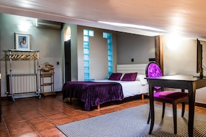 A bedroom with a bed, a desk, a chair, a radiator, a coat rack, and a window with blue panes.