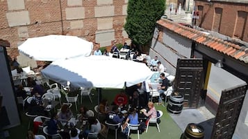 Un espacio al aire libre con mesas y sillas, rodeado de edificios de ladrillo y un árbol.
