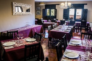 A restaurant with multiple tables set for dining, featuring a consistent tablecloth pattern and a classic chandelier.
