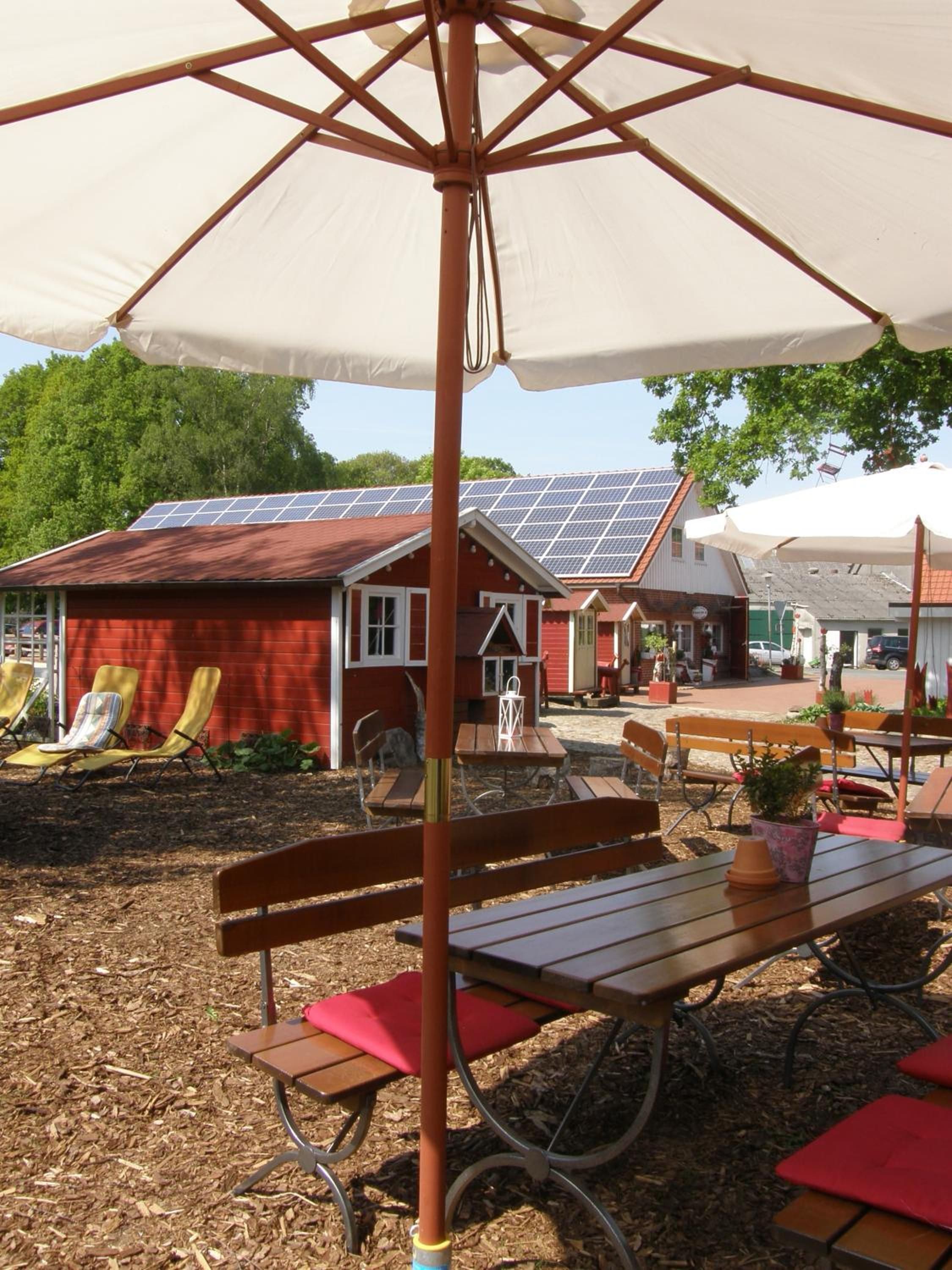 An outdoor seating area with tables and chairs, a large umbrella, and a building with solar panels in the background.