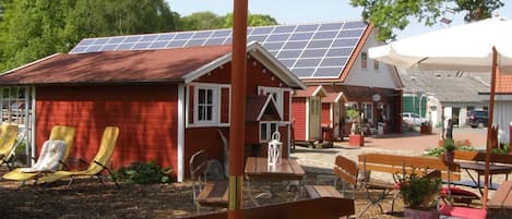 An outdoor seating area with tables and chairs, a large umbrella, and a building with solar panels in the background.