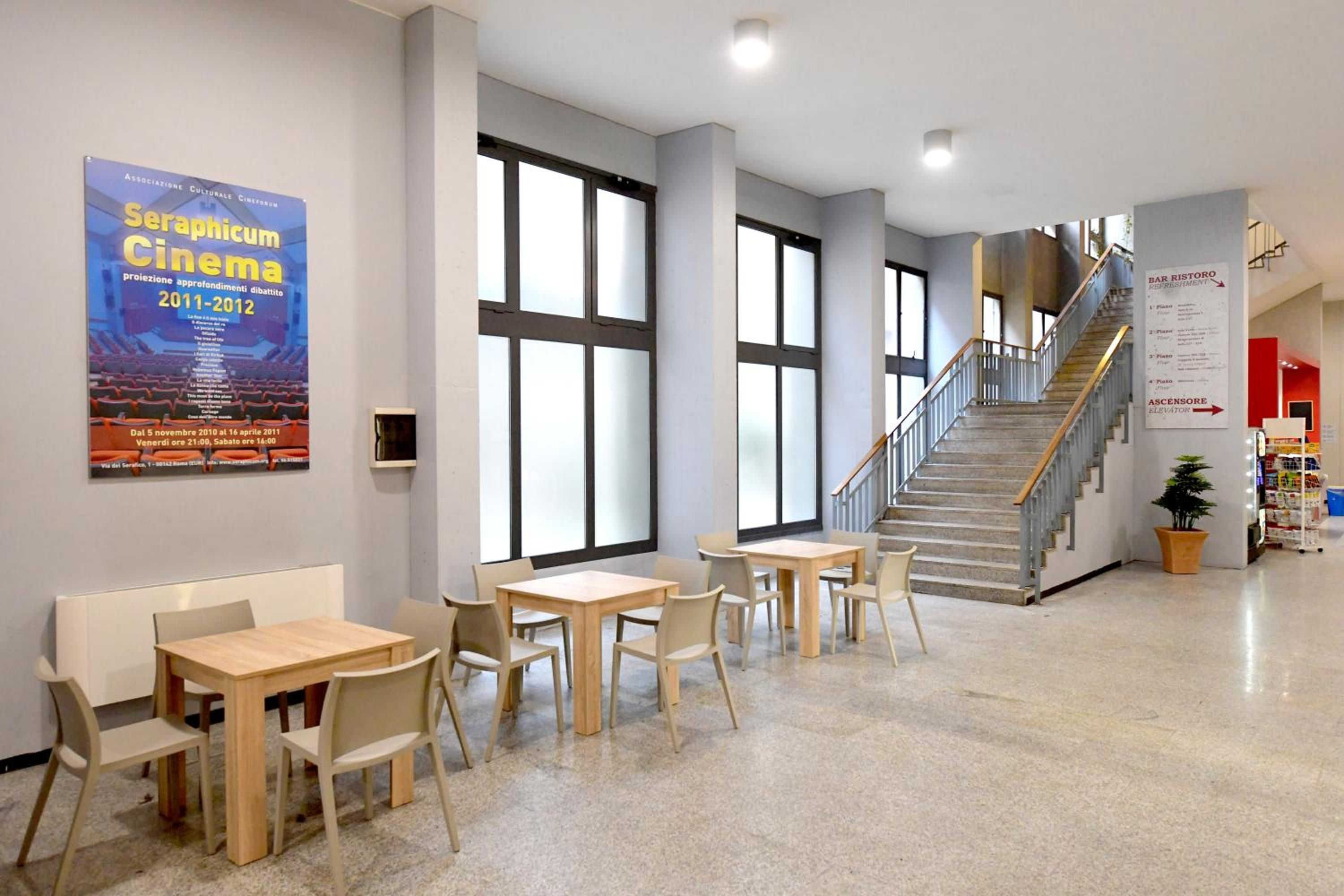 A spacious indoor area with a staircase, seating tables, and a poster on the wall.