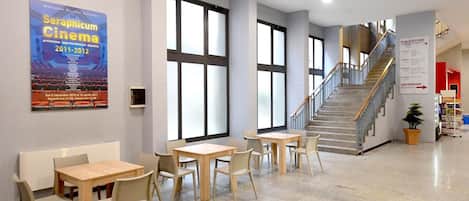 A spacious indoor area with a staircase, seating tables, and a poster on the wall.