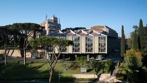 A modern building with a flat roof, large windows, and a parking area with trees in front.
