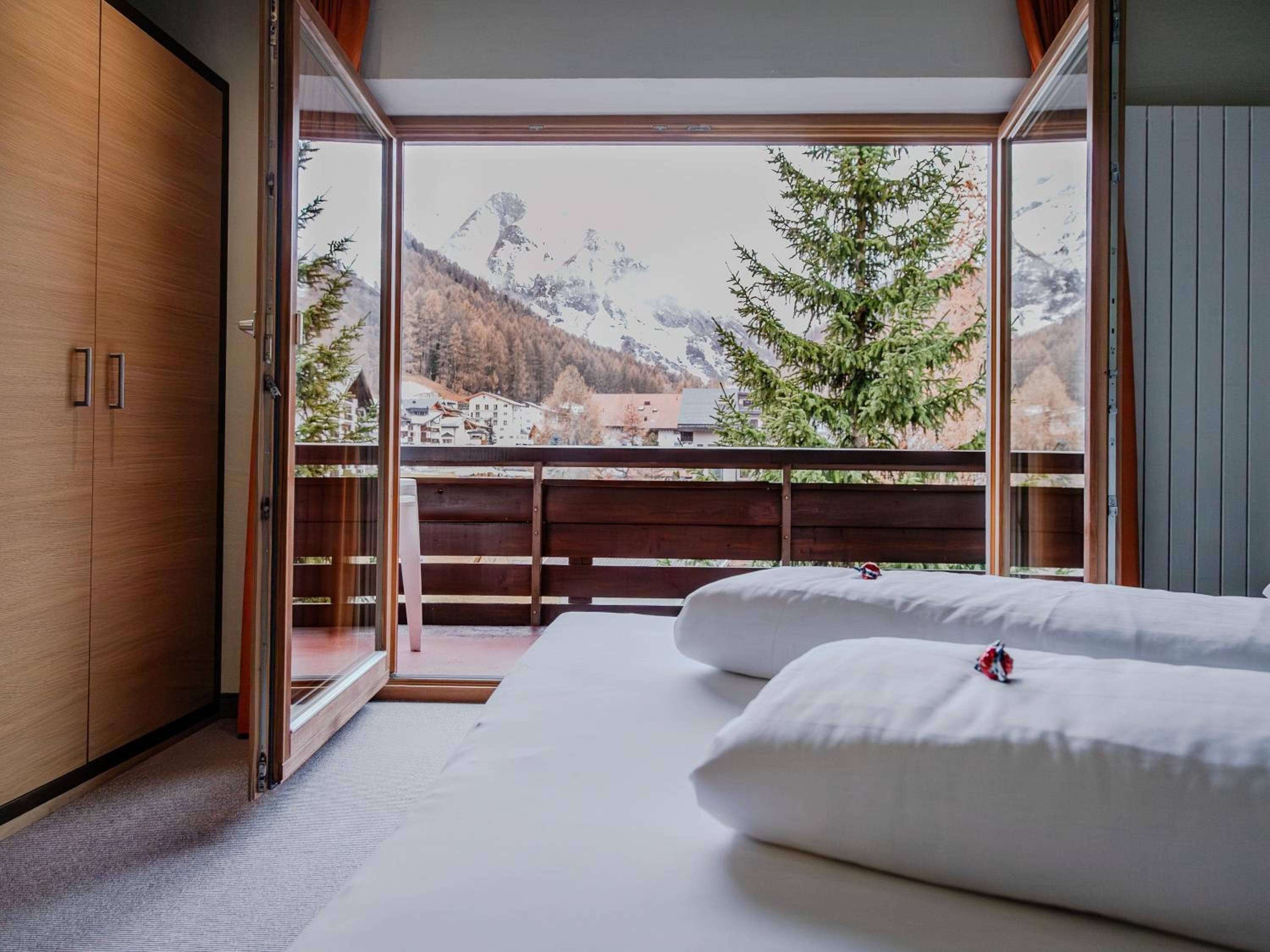 A bedroom with a large window, wooden wardrobe, and a bed with pillows.