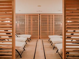 A room with wooden slatted partitions, a central aisle, and multiple beds aligned along the walls.