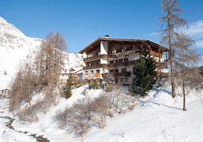 A multi-story hotel with a ski lift visible in the background, surrounded by snow-covered terrain and trees.