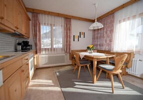 Una cocina con armarios de madera, una mesa de comedor con sillas, un radiador y una ventana con cortinas.