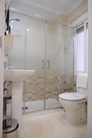 A bathroom with a glass-enclosed shower, a white sink, and a toilet.