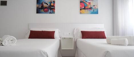 A hotel room with two beds, white bedding, red pillows, and two abstract paintings on the wall.