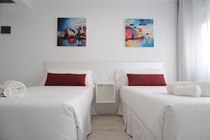A hotel room with two beds, white bedding, red pillows, and two abstract paintings on the wall.