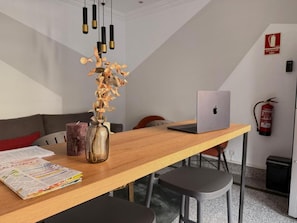 Un espacio de oficina moderno con una mesa de madera, una computadora portátil, un florero con flores secas y un extintor en la pared.