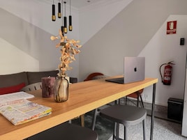 A modern office space with a wooden table, a laptop, a vase with dried flowers, and a fire extinguisher on the wall.