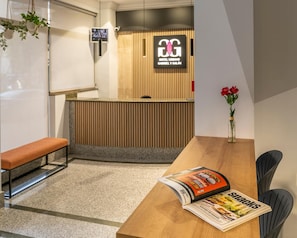Zona de recepción con diseño de paneles de madera, un banco, una revista sobre la mesa y un florero con flores.