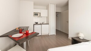 A compact hotel room with a kitchenette, a dining area with a table set for two, and a bed. - City Rv Sidence Nantes La Chantrerie (Nantes)