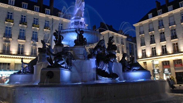 A nighttime view of a classical fountain with multiple statues, surrounded by illuminated buildings. - City Rv Sidence Nantes La Chantrerie (Nantes)